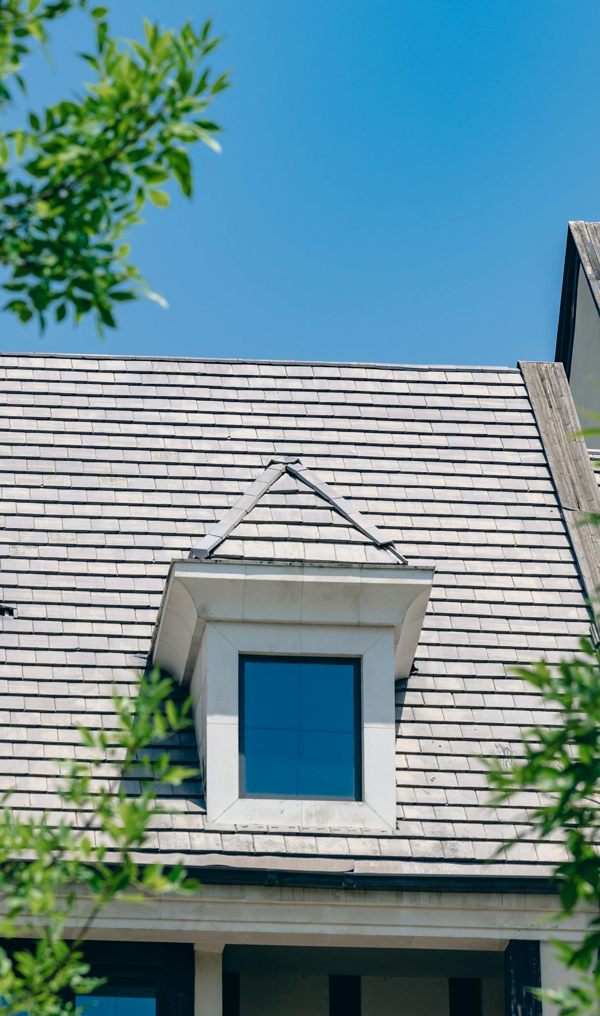 A Cape Cod style house roof with a prominent dormer window under a clear blue sky.